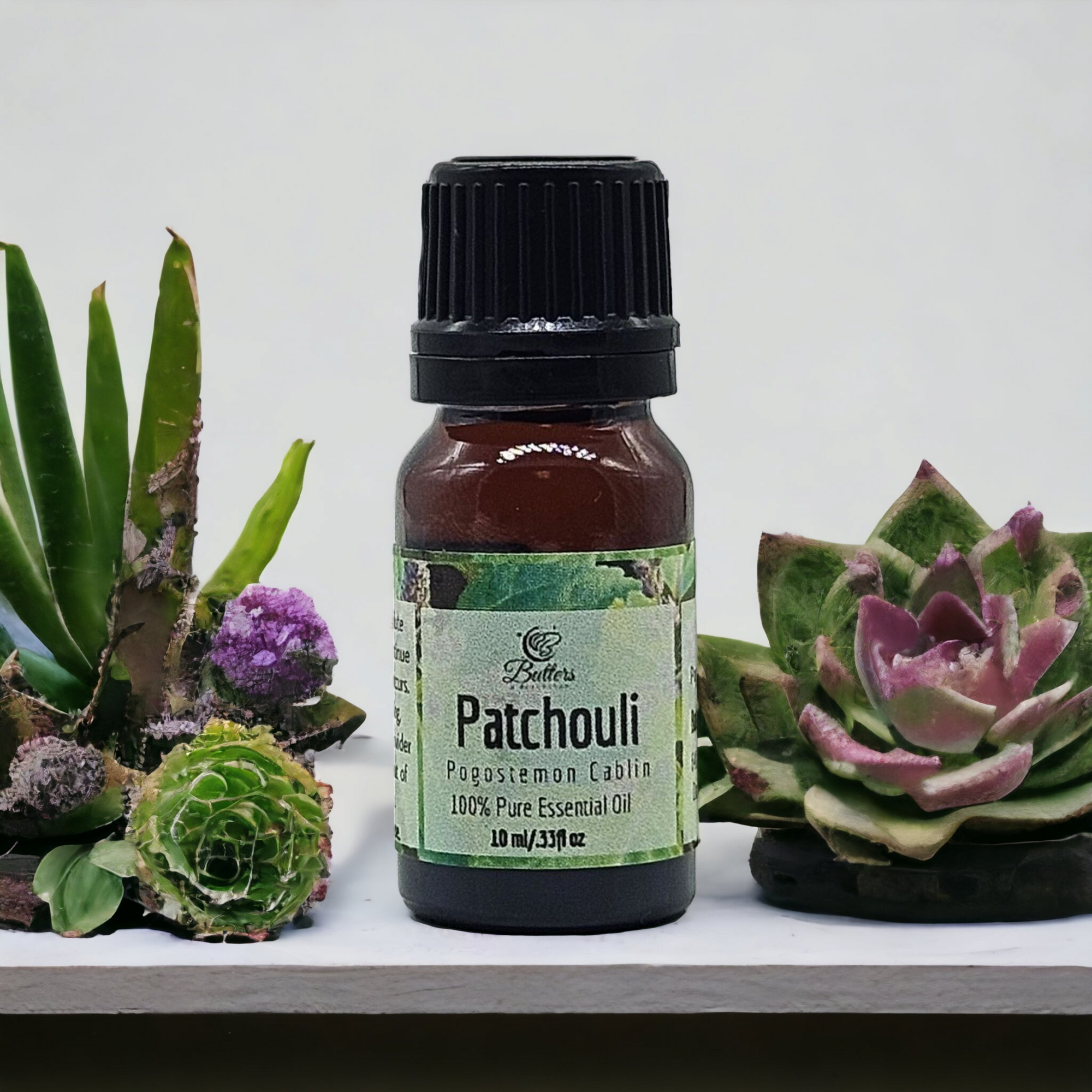 bottle of patchouli essential oil sitting in between green and pink succulents