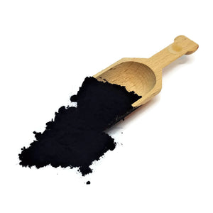 a pile of activated charcoal powder loaded on a wooden scoop. 
