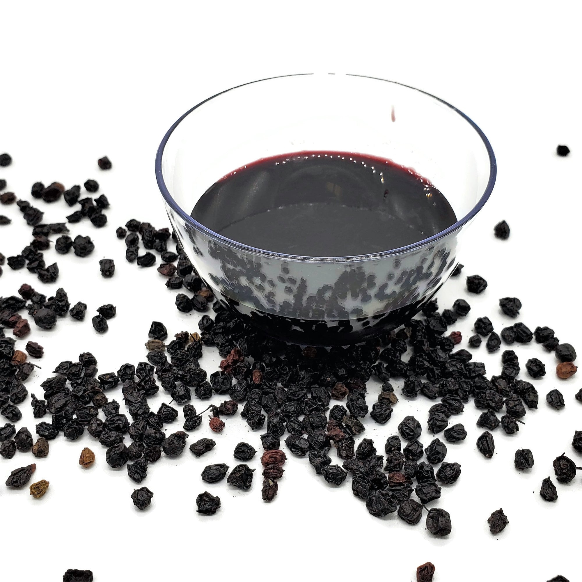 Bowl filled with elderberry syrup. The bowl is surrounded by dried whole elderberries. 